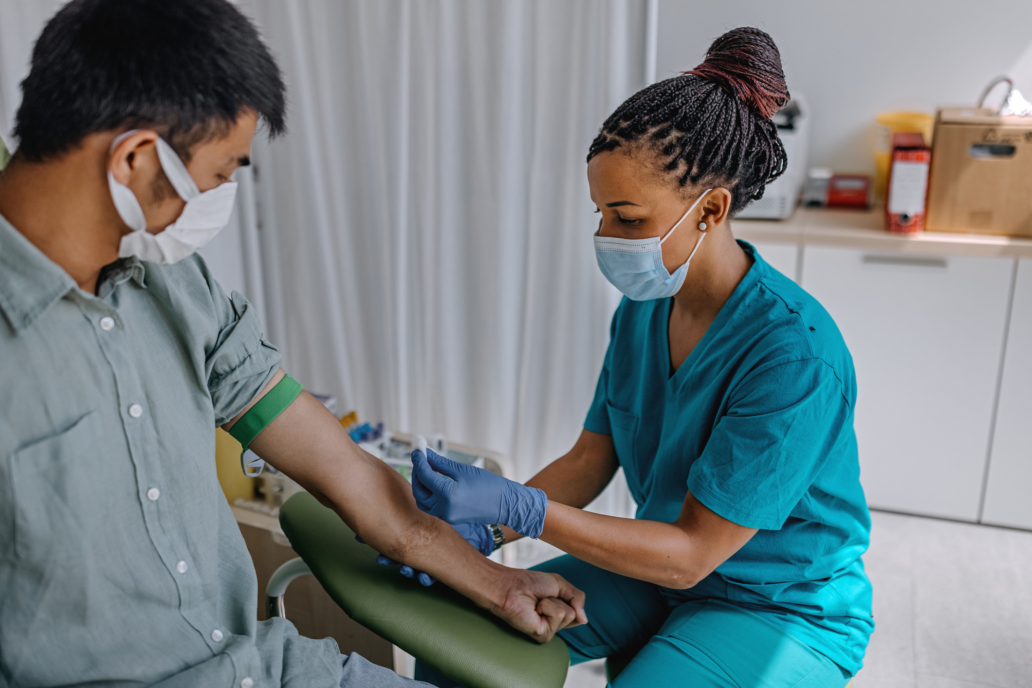 A nurse taking a blood sample from a young man's arm.