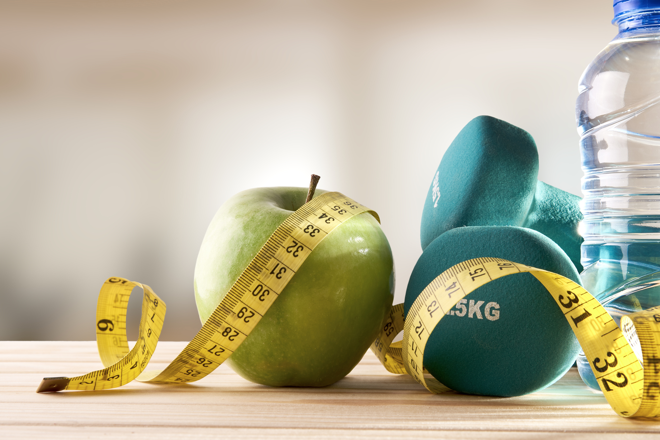 Image of an apple, dumbbells and a water bottle, all lightly wrapped with a tape measure