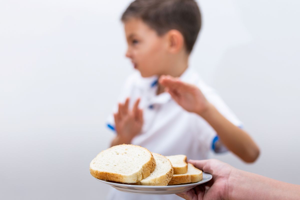 Child holding hands up refusing a plate of bread