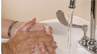 A pair of hands being washed next to a running tap in a sink