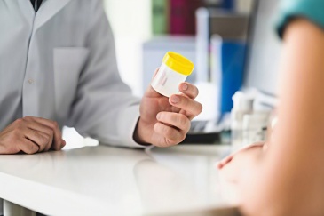 A male GP handing over an empty urine sample pot to a female patient