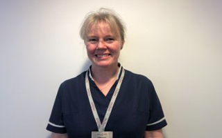 Dr Helen Hurst smiles in front of a white wall at her GP surgery. 