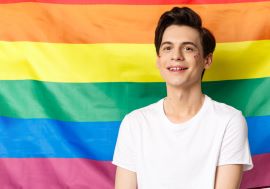 Beautiful gay man with glitter face smiling happy proud camera standing against rainbow